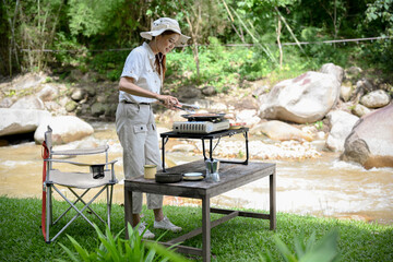 Female camper traveler grill some steaks on a portable outdoor picnic stove. Camping concept