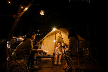A group of an Asian female teenagers enjoy camping and looking at the stars at night together - obrazy, fototapety, plakaty