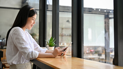 Fototapeta premium Beautiful Asian female relaxes sitting in the coffee shop and using tablet.