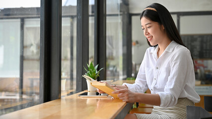 Attractive Asian woman relaxes sitting in the cafe and enjoy reading book.