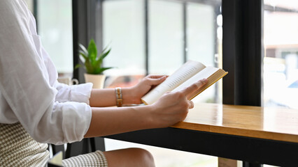 Obraz premium Pretty young Asian woman reading a book in the coffee shop. cropped