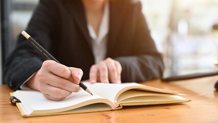 A businesswoman writing something with pencil on her notebook. cropped image
