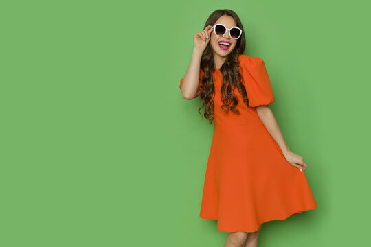 Happy young woman in orange mini dress is posing in sunglasses and shouting.