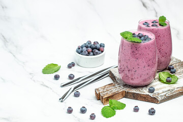 two glasses of fresh berries with yogurt smoothies fresh blueberries or bilberry on a light...
