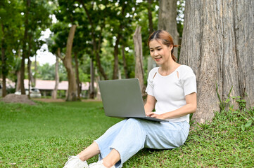 Attractive Asian female or college student sits under the tree in the park using her laptop.