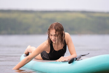 A beautiful girl is floating on a supboard on a river. Young woman supsurfing at sunrise.