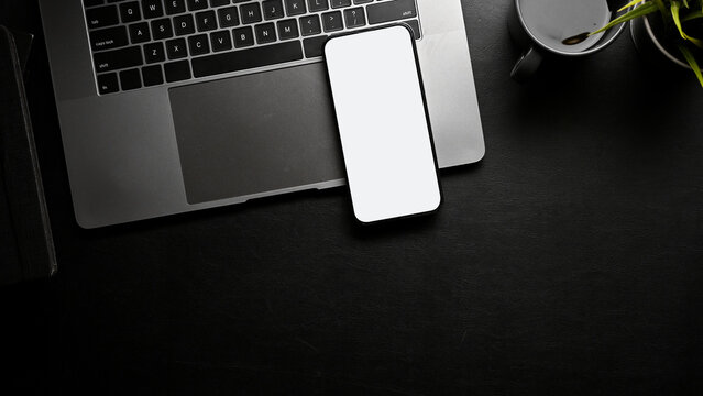 A smartphone white screen mockup, laptop and copy space on black workspace