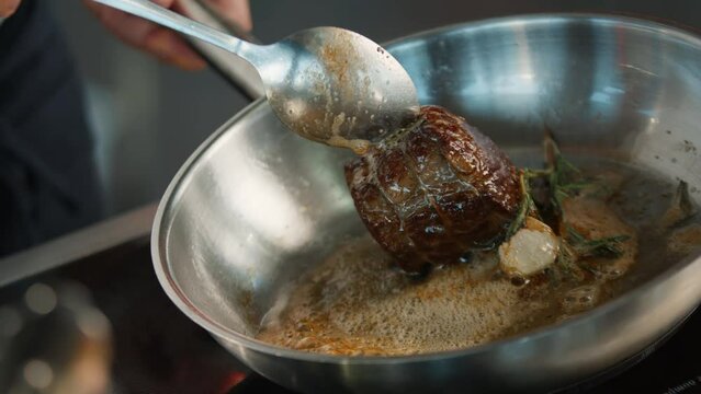 Close-up: Chef pouring sauce over filet mignon while cooking