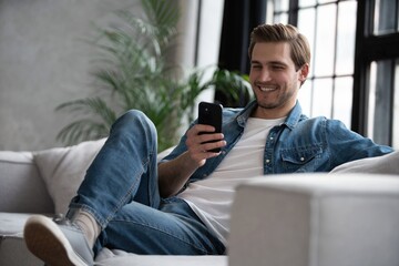 Attractive smiling young man wearing casual clothes sitting on a couch at the living room, using...