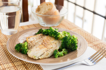 fried fillet of sea bass with garnish of broccoli on black warm stone plate