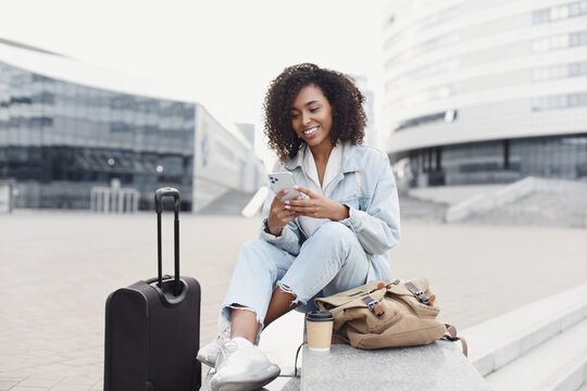 Beautiful woman tourist with suitcase luggage using smart phone outdoor. Smiling student girl going on travel. Business travel, student lifestyle, connection, tourism concept