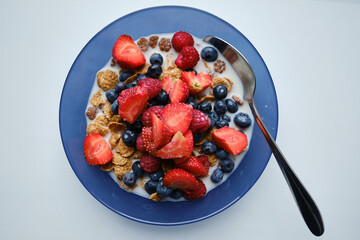 Healthy breakfast in bowls with muesli, corn flakes, milk fresh raspberry, blueberries and strawberries. Health and diet concept
