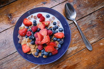 Healthy breakfast in bowls with muesli, corn flakes, milk fresh raspberry, blueberries and strawberries. Health and diet concept
