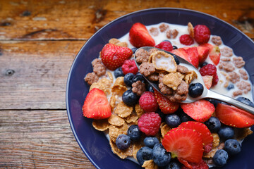 Healthy breakfast in bowls with muesli, corn flakes, milk fresh raspberry, blueberries and strawberries. Health and diet concept
