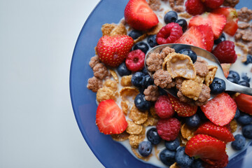 Healthy breakfast in bowls with muesli, corn flakes, milk fresh raspberry, blueberries and strawberries. Health and diet concept
