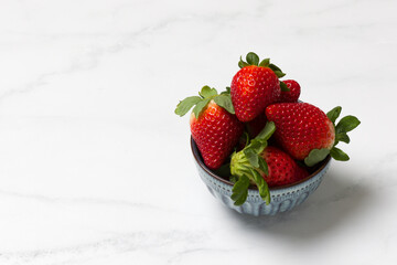 Strawberries with leaves in a small blue bowl with a marble kitchen counter background. Food photography. Editorial. 2
