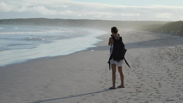 Young Female Backpacker Taking Photograph Of Waves On Tortuga Bay In The Galapagos. Slow Motion