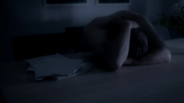 Depressed man leaning over and crying over bills at night. Static