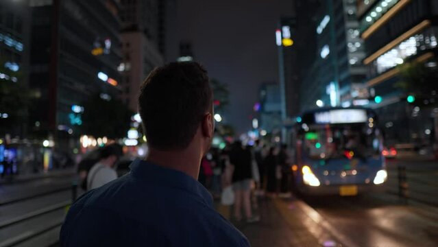 Back view of a man at bus stop at night Seoul waiting for transportation. Closeup Unrecognizable busy man looking at his wristwatch to check time at Gangnam Station in slow motion