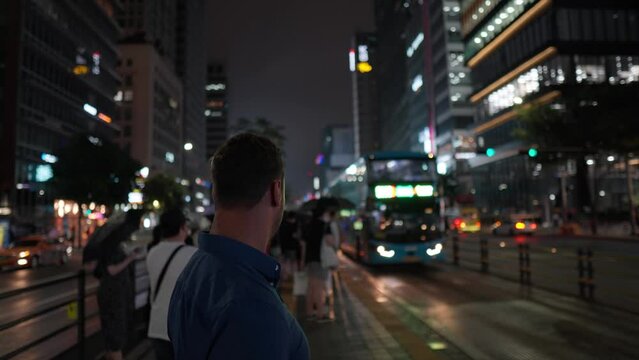 Face close-up of young man searching his bus at station when double-decker night bus depart from platform in the middle of Gangnam-daero road in Seoul