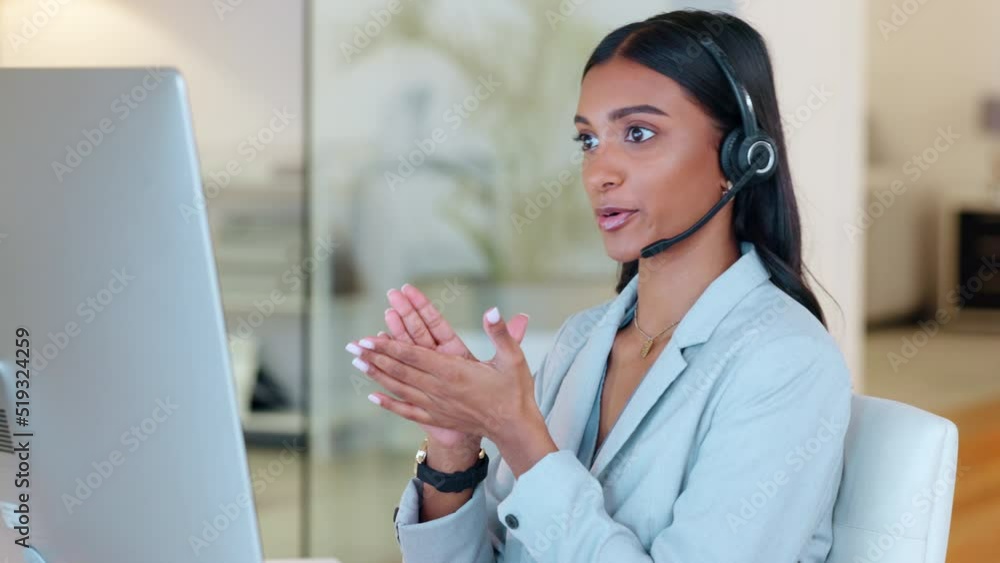 Poster Call center agent talking and advising clients while working on a desktop computer in an office alone at work. Young Indian customer service agent wearing a headset and giving help to people