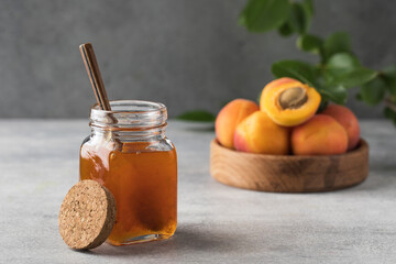 A jar with apricot jam and a spoon close-up on a gray. Fruit preservation.