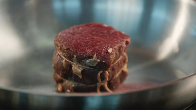 Close-up of a raw filet mignon being cooked in a frying pan