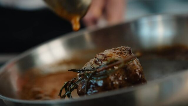 Close-up: Chef pouring sauce over filet mignon while cooking
