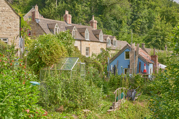 A row of Cotswold stone cottages with their back gardens