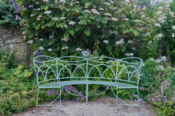 Ornate green metal garden bench surrouned by flowers