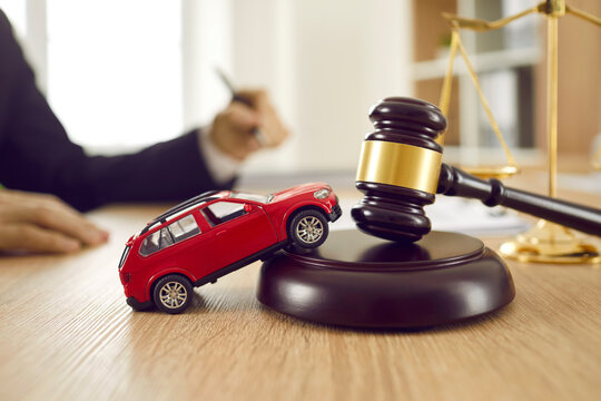 Little red toy automobile on table with sound block and gavel. Small car model on wooden desk with judge's hammer. Car accident, drunk driving, lawsuit, court of law, justice, lawyer services concept