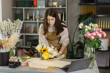 Gardeners in the flower shop make bouquet for a holiday and wraps it in kraft paper. Family flowers business. Lifestyle flower shop. Beautiful flower composition. Detail. Close up.