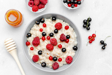 Oatmeal porridge with summer raspberry, currant berries,honey. Porridge oats in bowl with fruits. Healthy food breakfast,lifestyle,dieting, proper nutrition.Top view flat lay on gray table background