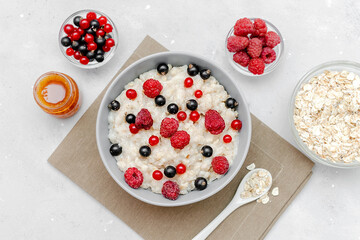 Oatmeal porridge with summer raspberry, currant berries,honey. Porridge oats in bowl with fruits. Healthy food breakfast,lifestyle,dieting, proper nutrition.Top view flat lay on gray table background