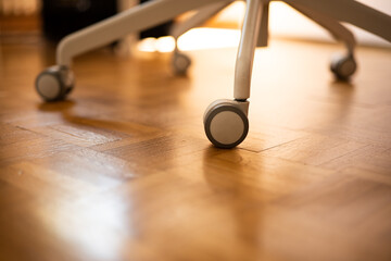 Office arm wheelchair legs on a laminated wooden floor. Close up shot, sunlight illuminating the...