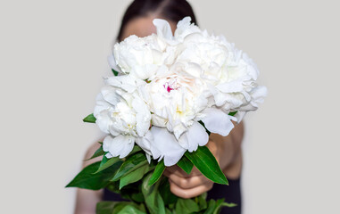 white peonies bouquet in woman hand and big paper envelope.flowers delivery,buy concept,shop store.girls hand raised up isolated on beige light background.beautiful peony flowers.mother women day