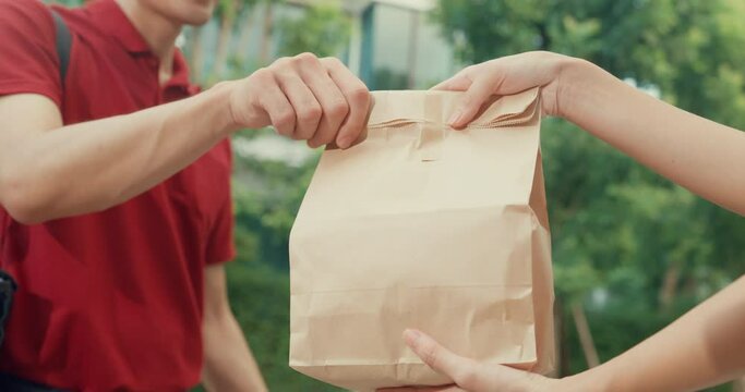 Close-up Young happy Asian delivery man with bicycle in red uniform carry case box knock door home shopping online food paper bag to woman in front of door at house. express food delivery concept.
