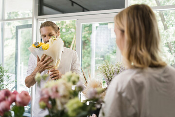 A young bearded man buys a beautiful bouquet of flowers for a girl's holiday in a cozy flower shop. Floristry and bouquet making in a flower shop. Small business.