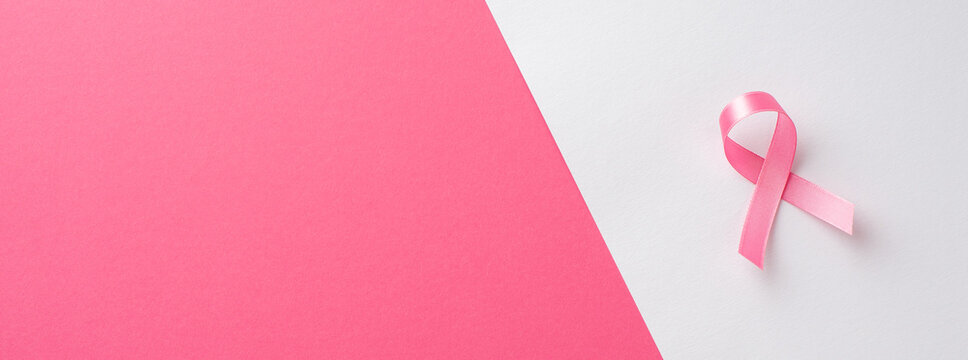 Top view photo of pink ribbon symbol of breast cancer awareness on bicolor pink and white background with empty space
