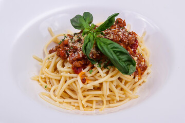 close-up spaghetti noodles topped with pieces of meat mixed with cheese and green vegetables served on a white plate