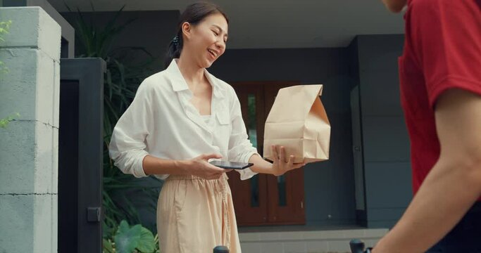 Young happy Asian woman accept paper bag from delivery man with bicycle in red uniform carry case box scan QR code payment on smartphone in front of house. express food delivery concept.