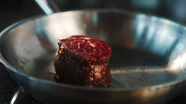 Close-up of a raw filet mignon being cooked in a frying pan