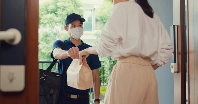 Young Asian delivery man wear mask in blue navy uniform carry case box knock door home online shopping paper bag to woman in front of door lady scan QR code payment on smartphone at house concept.