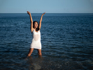 Joyful young Hispanic woman splashing water in sea