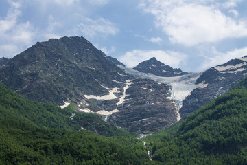 A beautiful panoramic landscape - the slopes of high mountains with snowy peaks and glaciers against a cloudy sky in the Elbrus region in the northern Caucasus in Kabardino-Balkaria