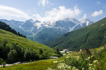 Pastoral landscape - green hillsides and high mountains with snowy peaks over a valley with alpine meadows on a clear sunny summer day in the Elbrus region in the North Caucasus in Russia