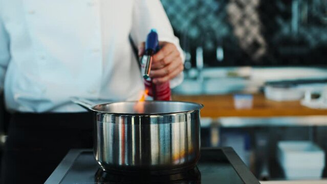 The chef sets fire to the dish in the professional kitchen of the restaurant. The process of cooking food with fire.