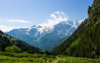 Pastoral landscape - green hillsides and high mountains with snowy peaks over a valley with alpine meadows on a clear sunny summer day in the Elbrus region in the North Caucasus in Russia