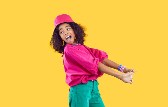 Cheerful funny stylish african american teen girl having fun on vivid yellow background. Happy energetic kid girl in trendy bright colored clothes having fun and fooling around laughing out loud.
