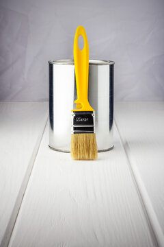 yellow brush with a can of paint on a white wooden background close-up